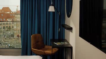 Hotellihuone, josta avautuu näkymä kaupungin siluettiin, ruskea nahkainen nojatuoli, pieni pöytä, jonka päällä on lehti, ja musta lamppu.