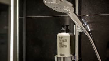 A shower with a handheld showerhead and a bottle of body wash.