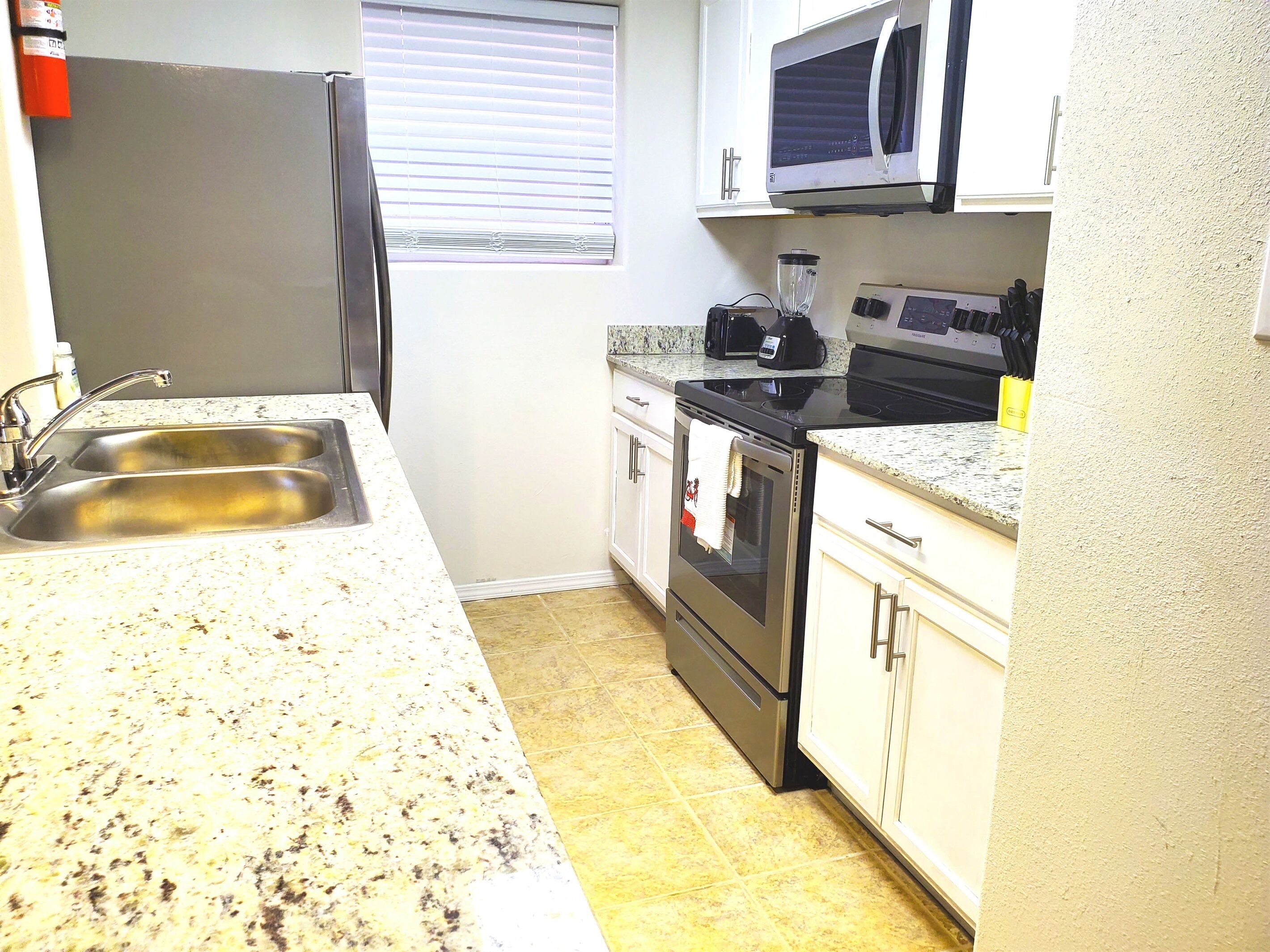 A kitchen with a stainless steel refrigerator, double sink, microwave, stove, and oven.