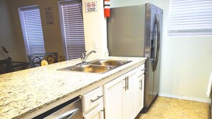 A kitchen with a stainless steel refrigerator, a double sink, white cabinets, and a granite countertop. - Sun Ray #1A - Pet Friendly, 3min Walk to Beach (South Padre Island)