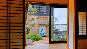 A traditional Japanese interior with sliding doors, a tatami mat floor, and a view of a building with a Japanese-style sign.