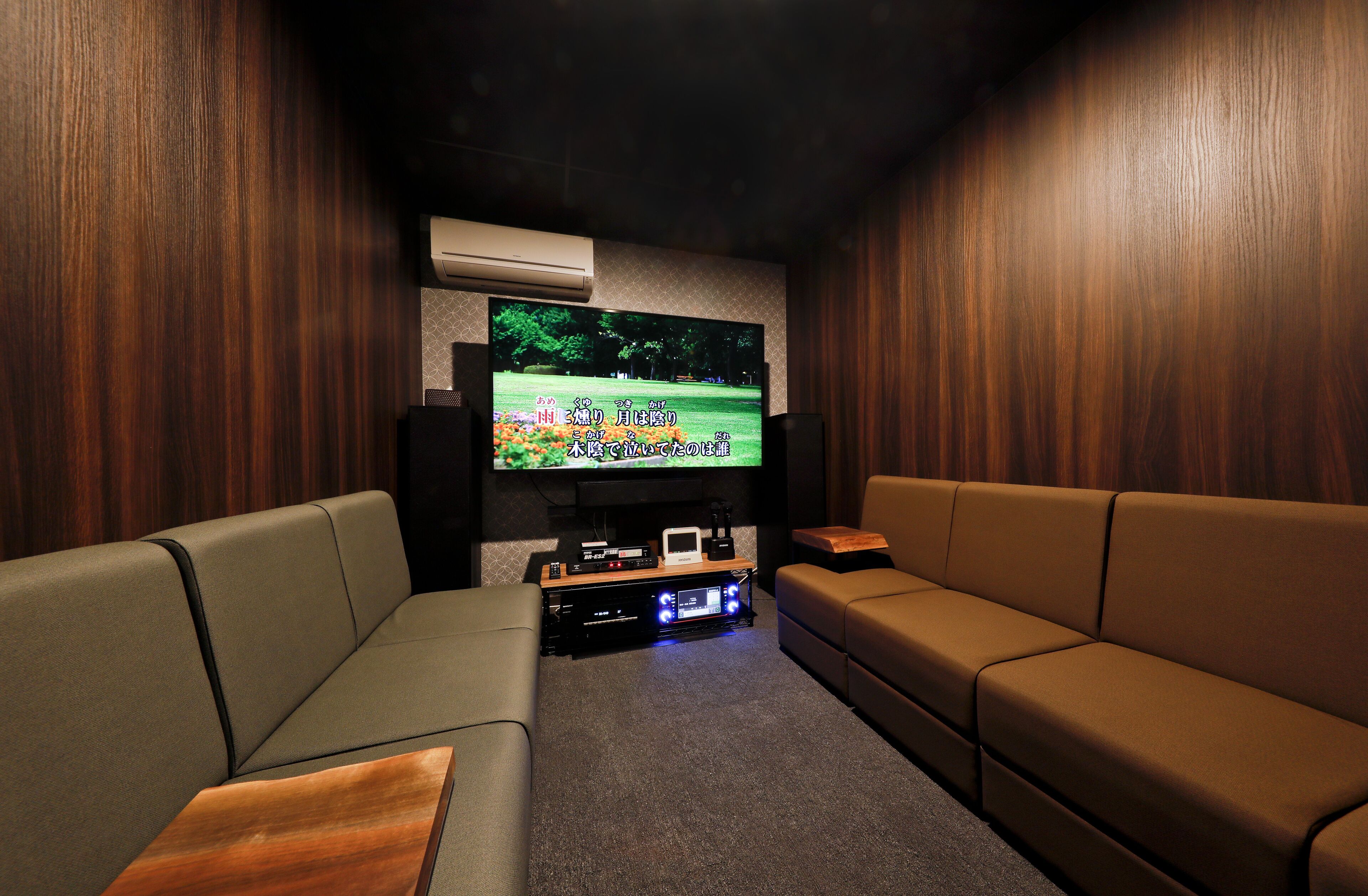 Una sala de cine en casa con un televisor de pantalla plana grande montado en la pared, rodeada de paneles de madera. Hay dos sofás de cuero y una mesa de centro de madera en el centro.