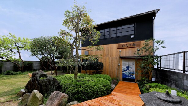 A traditional Japanese house with a wooden exterior, a stone pathway leading to the entrance, and a small garden with rocks and shrubs.