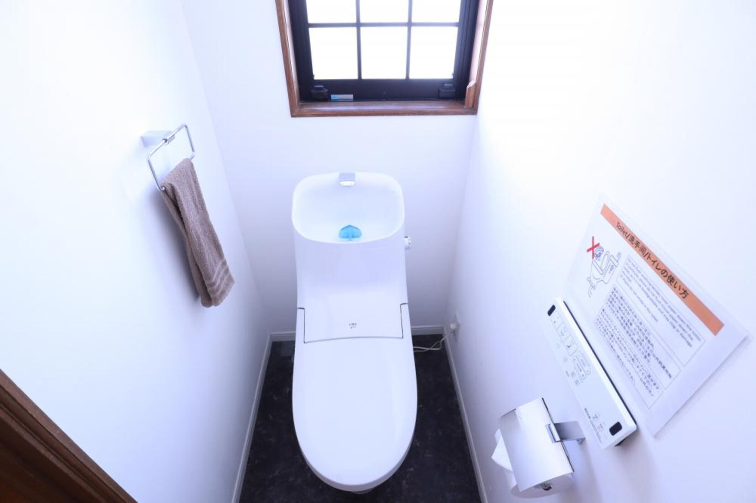 Eine kleine, weiße Toilette mit Fenster darüber, ein Handtuch an einem Halter und ein Schild an der Wand.