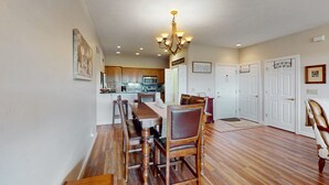 A spacious dining area with a wooden table and chairs, a chandelier, and a kitchen in the background. - Relaxing condo with sweeping valley views, deck, and fireplace (Sugar Mountain)