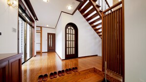 Un pasillo amplio con suelo de madera, una escalera y una fila de zapatos ordenados sobre un banco de madera.