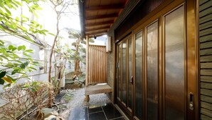 Una entrada tradicional al estilo japonés con una puerta de madera y un pequeño sendero de piedra que lleva a un banco.