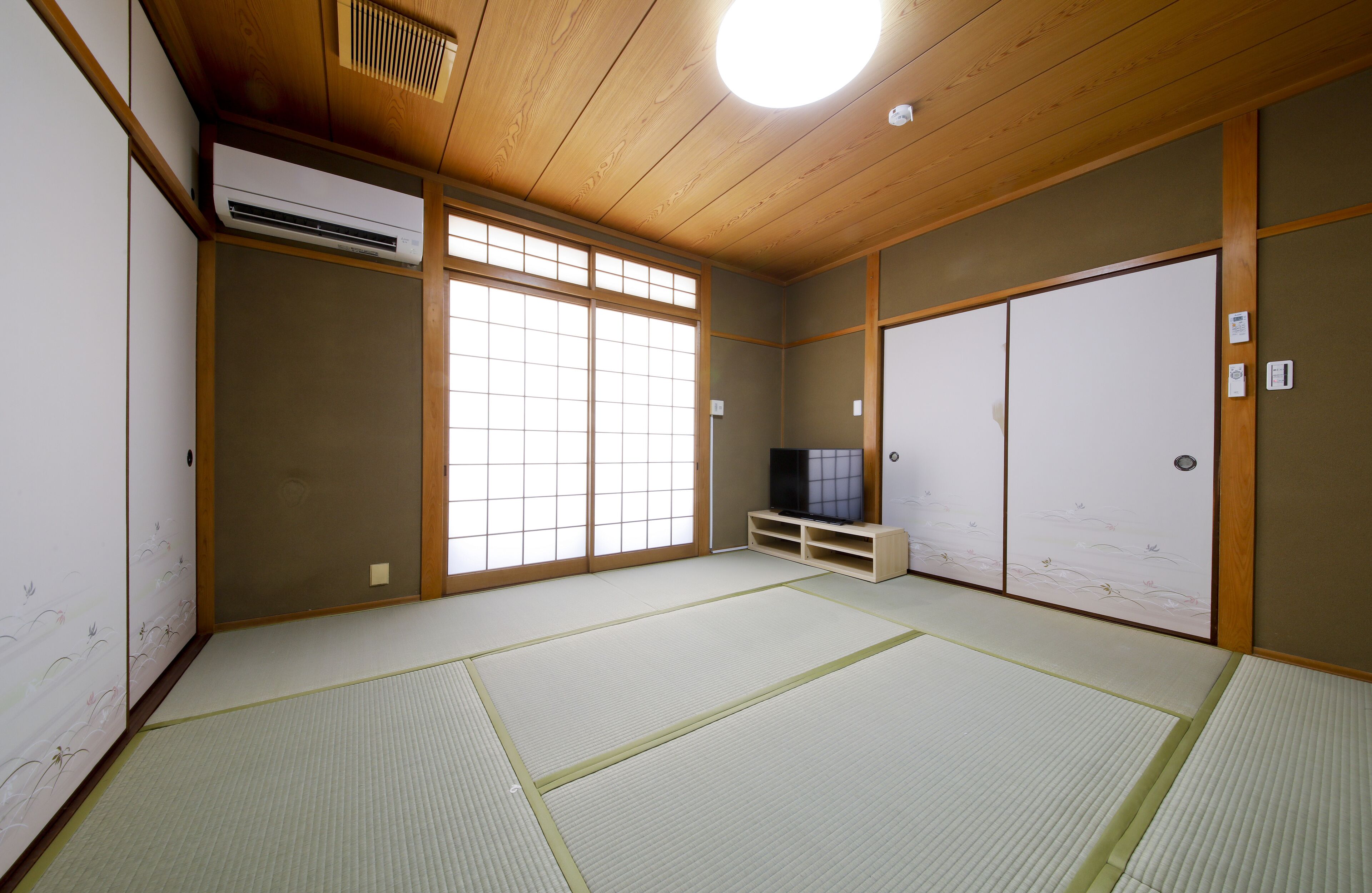 A traditional Japanese room with tatami flooring, sliding doors, and a television on a low stand.