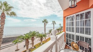 Un balcón con vista al mar, palmeras y una mesa de vidrio con un sombrero.