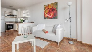 Una cocina moderna con armarios blancos, un comedor con mesa y taburetes blancos, un sofá blanco y una lámpara de pie.