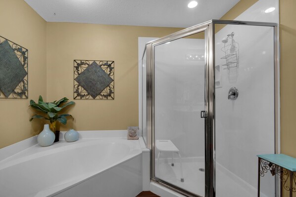 Une salle de bain avec une douche à parois de verre, une baignoire blanche, des éléments décoratifs sur les murs et une petite plante.