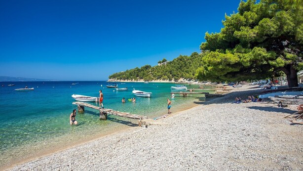 Una playa con agua turquesa cristalina, barcos y gente.