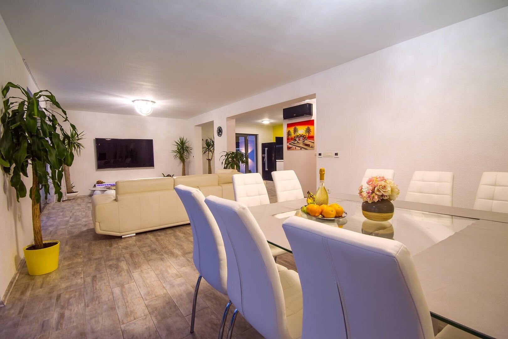 A modern living room with a sofa, a dining table with chairs, and a TV mounted on the wall.
