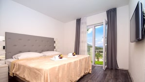 Habitación de hotel con cama, mesita de noche, televisor montado en la pared y balcón con cortinas.
