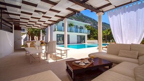 Un espacio exterior moderno con piscina, mobiliario blanco y vistas a la montaña.