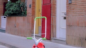 Un tricycle rouge et vert est garé devant un bâtiment en briques, avec une porte jaune et une porte blanche.