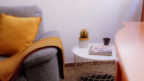 Un canapé gris avec un plaid de couleur moutarde, une petite table ronde sur laquelle se trouve un pot de fleurs, un magazine et un vase foncé.