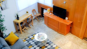 Un espace de vie compact comprenant un canapé, une petite table basse ronde, un téléviseur posé sur un meuble en bois, une table à manger avec des chaises et une cheminée.