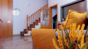 Une pièce avec un lit recouvert d’une couverture jaune, un escalier en bois et une fenêtre. Un coussin jaune est posé sur le lit.