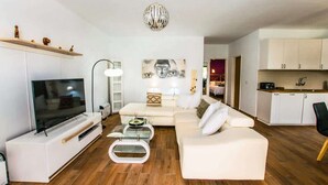 Ett modernt vardagsrum med en platt-TV, en soffa, ett soffbord och en hänglampa.