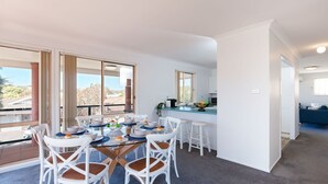 A modern kitchen with white cabinets, a dining area with a glass table, and a view of the outdoors. - Redman Views Unit 1  13 Redman Place (Soldiers Point)