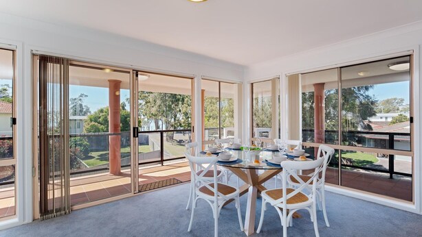 A dining area with a table set for four, large sliding glass doors, and a view of the outdoors. - Redman Views Unit 1  13 Redman Place (Soldiers Point)