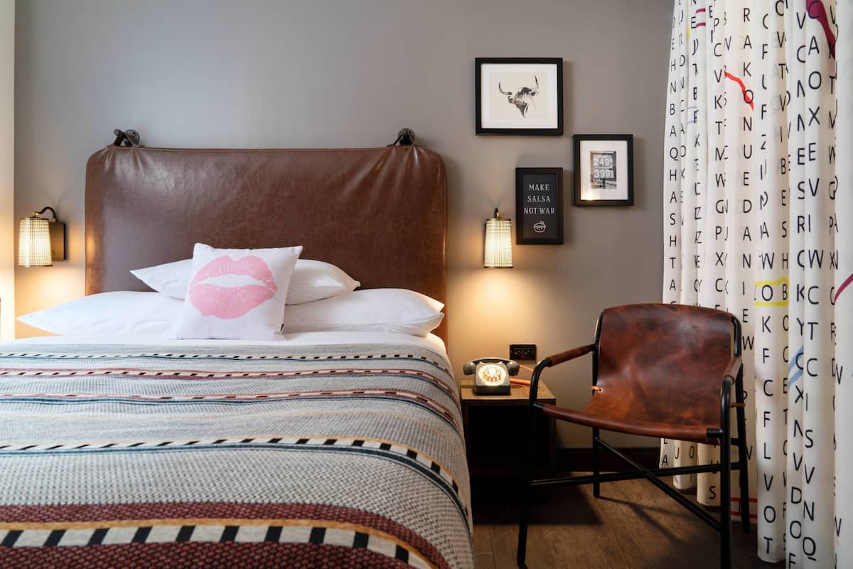 A neatly arranged hotel room with a large bed, a chair, a nightstand with a lamp, and framed pictures on the wall.