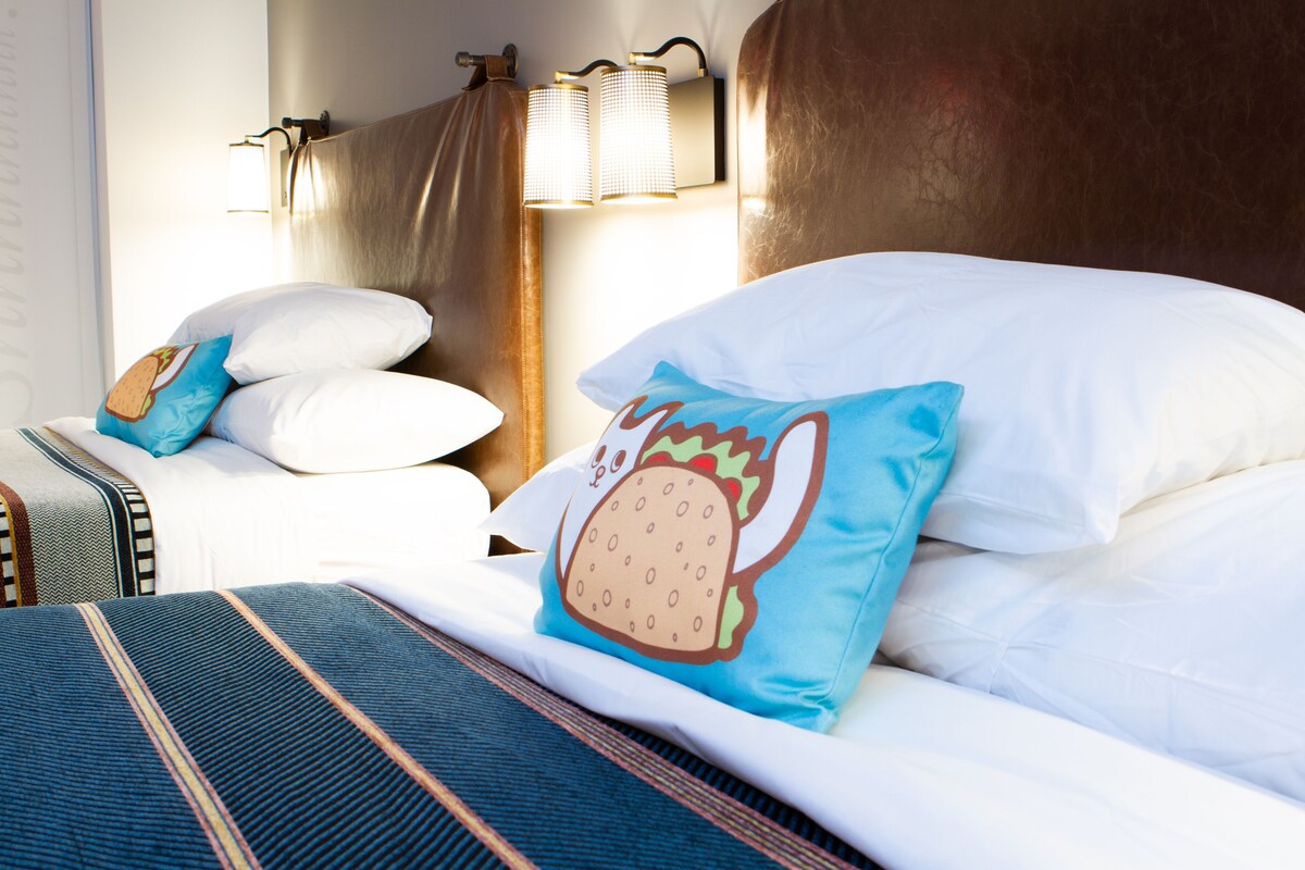 Habitación de hotel con una cama grande, dos almohadas, cabecera y una lámpara fijada a la pared.