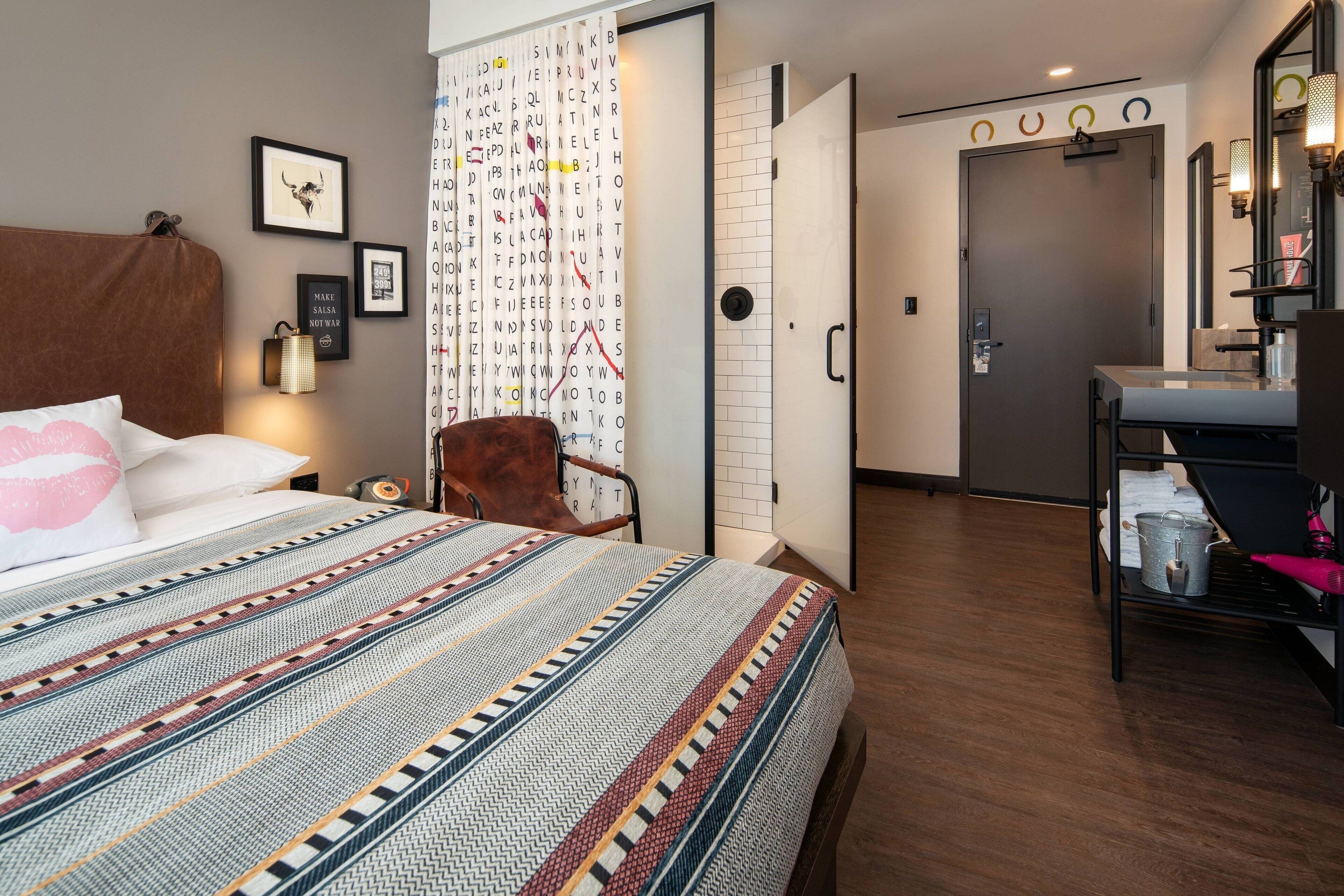 A hotel room with a bed, a chair, a desk with a mirror, and a wardrobe.