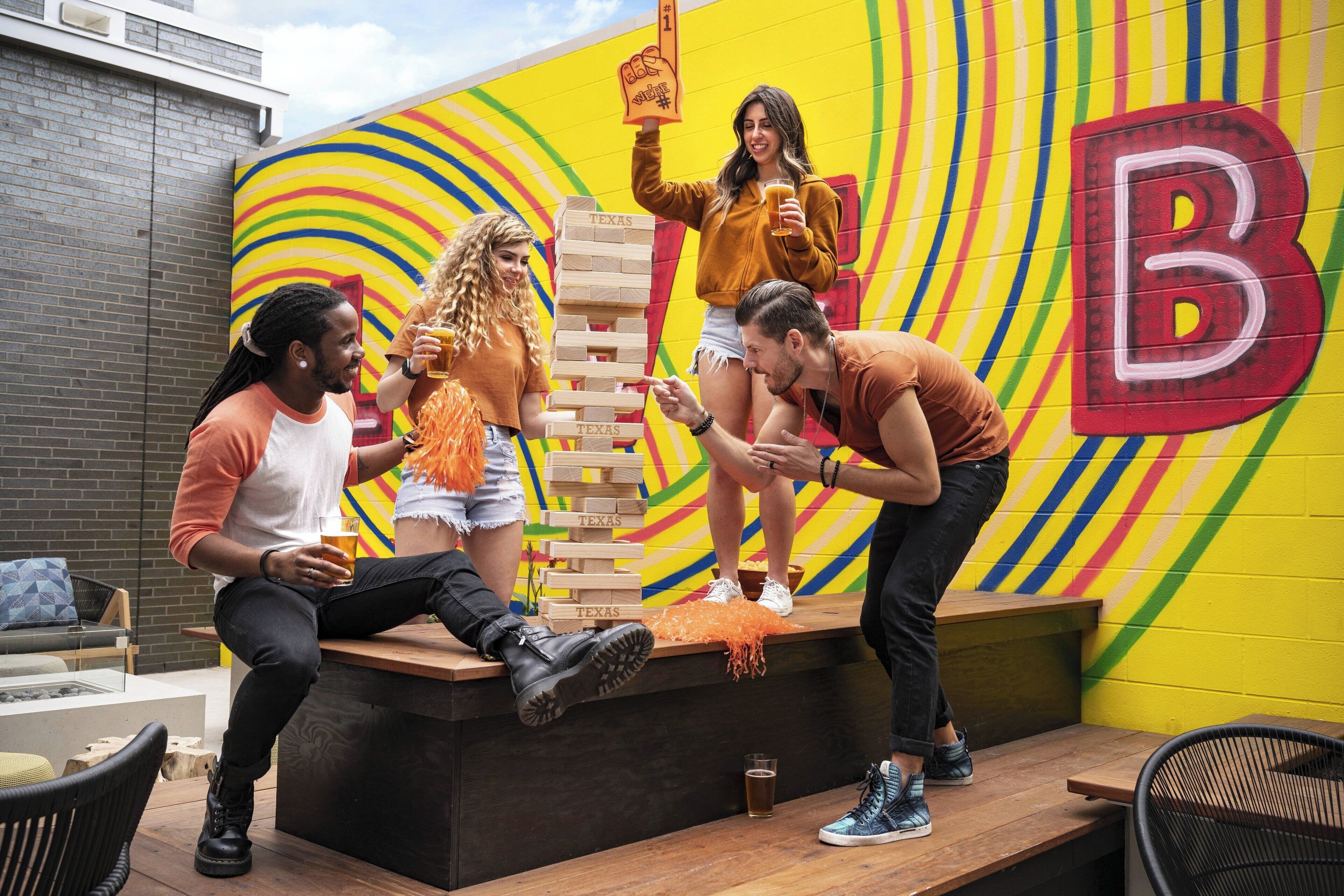 A group of people playing Jenga on a wooden platform with a colorful mural in the background.