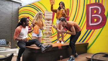 A group of people playing Jenga on a wooden platform with a colorful mural in the background.