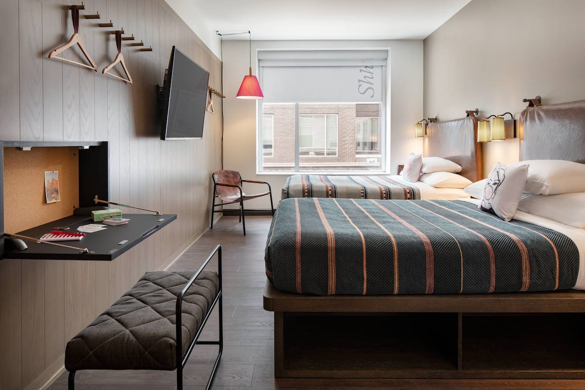 A modern hotel room with a bed, a desk, a chair, and a bench.