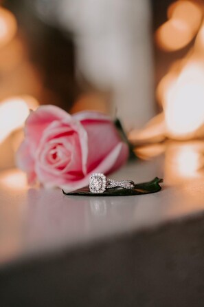 A delicate diamond ring sits beside a beautiful rose.