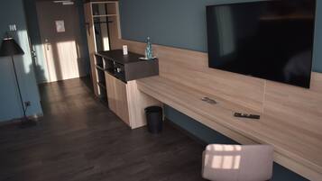 Una habitación de hotel moderna con un escritorio de madera, un televisor de pantalla plana, una silla y un cesto de basura.