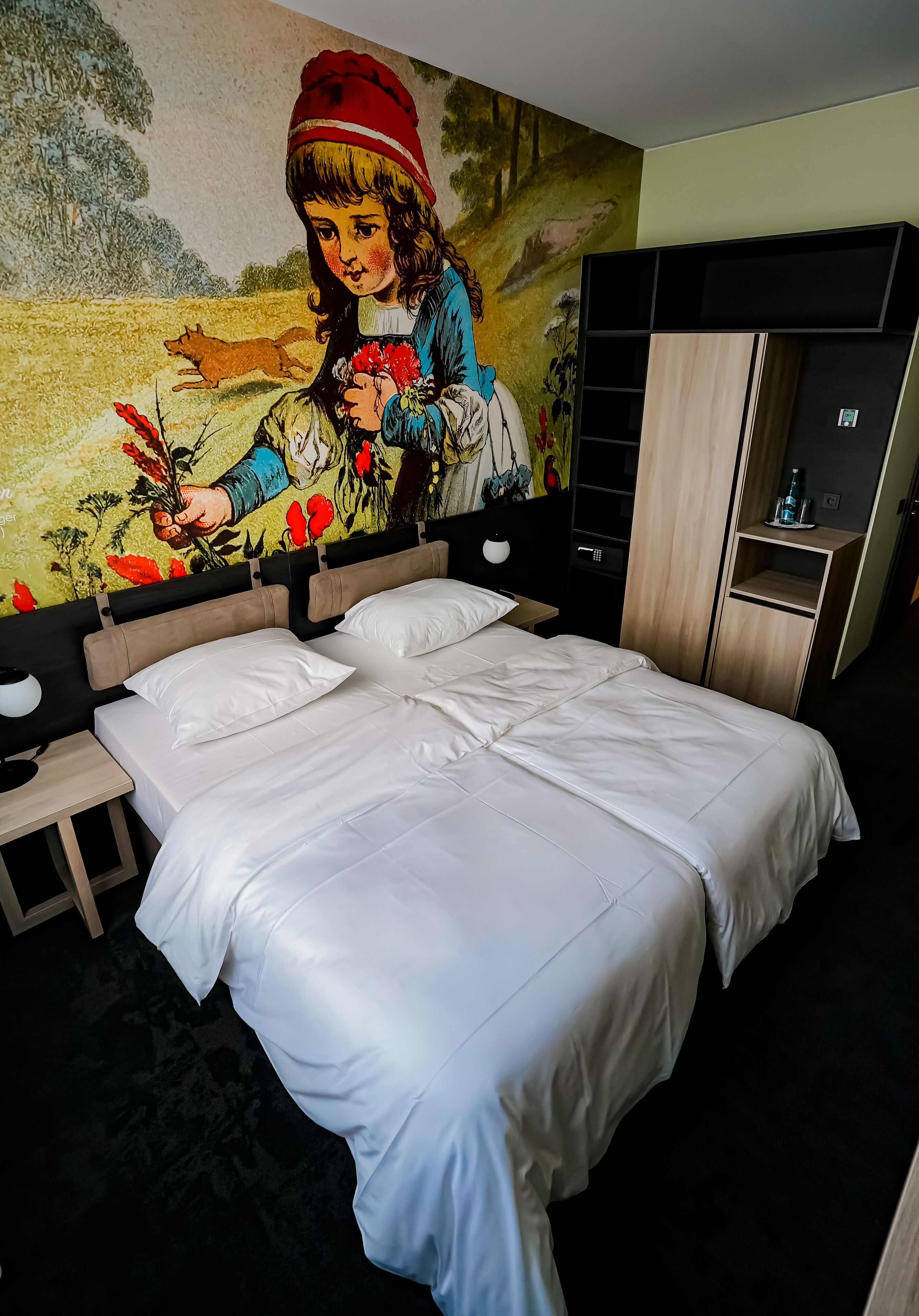 Une chambre d’hôtel avec un grand lit, une table de chevet, une armoire en bois et une fresque murale.