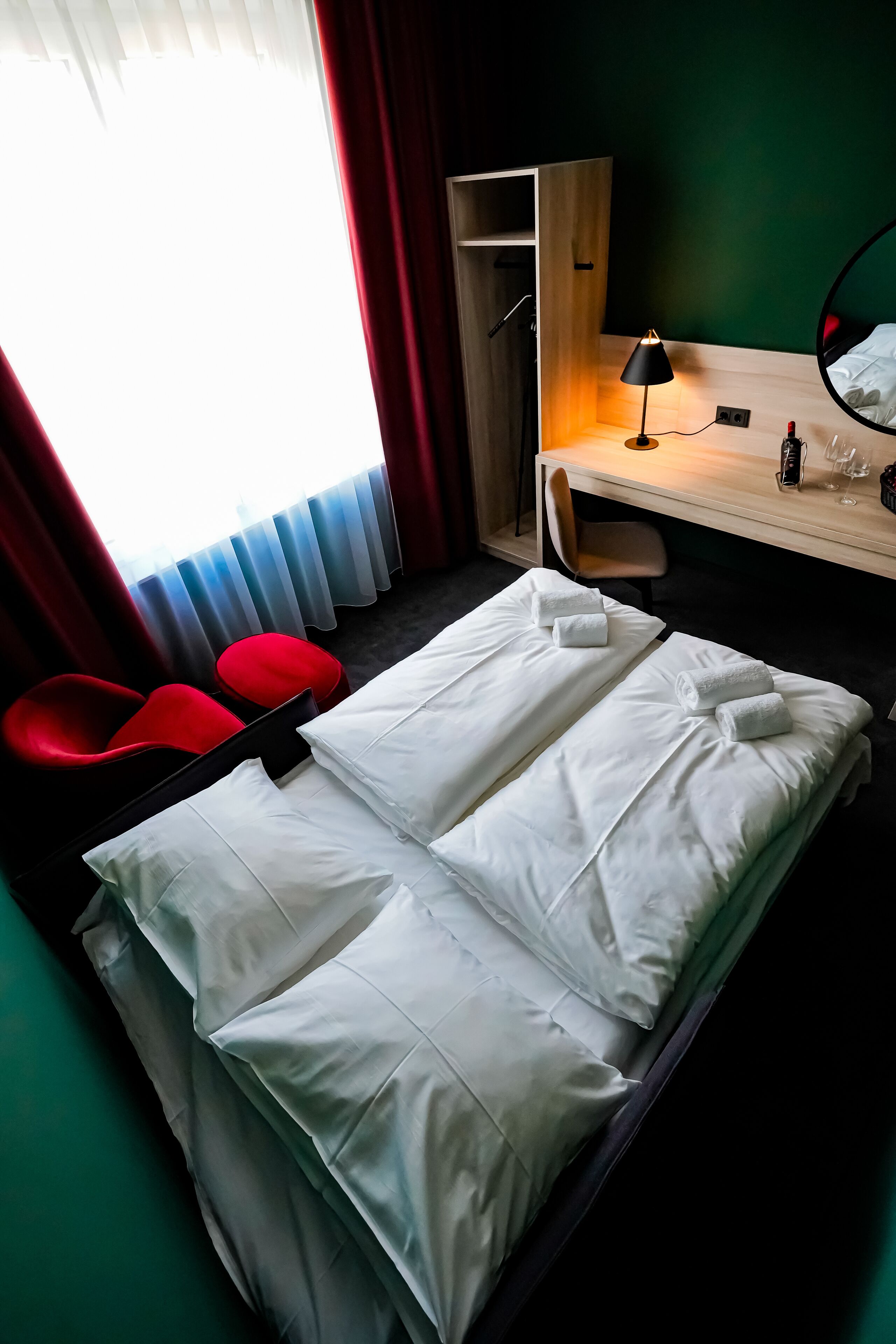 A hotel room with a bed, a desk, a chair, and a red chair.