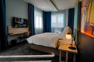 A modern hotel room with a large bed, a desk, and a TV on the wall.