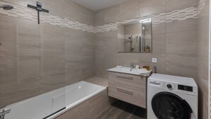 Ein modernes Badezimmer mit Badewanne, Waschbecken, Spiegel und Waschmaschine.