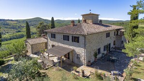 Una casa in pietra con tetto in tegole, un piccolo edificio adiacente e un cortile pavimentato con posti a sedere all'aperto.
