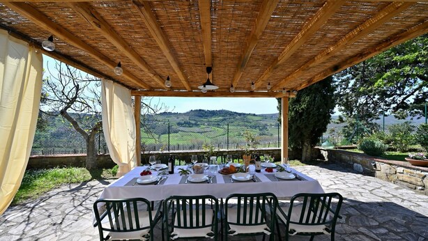 Zona pranzo all'aperto con tavolo imbandito per quattro, affacciata su un paesaggio suggestivo.