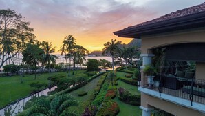 Jardín ajardinado con fuente de agua, palmeras y vista al mar al atardecer.