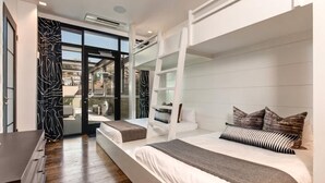 Una habitación de hotel moderna con literas, un escritorio y un puerta de vidrio que da a un balcón.