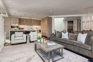 Ein modernes Wohnzimmer mit einem grauen Sofa, zwei Sesseln, einem Couchtisch und einer Küche im Hintergrund.
