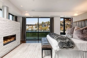 Sala de estar moderna com lareira, sofá com manta de pele e uma janela ampla com vista para um bairro residencial.