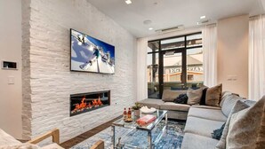 A modern living room with a stone fireplace, a large window, and a sofa. - Abode at Parkite #24, hot tub, balcony overlooking Main Street, gym, luxury condo (Park City)