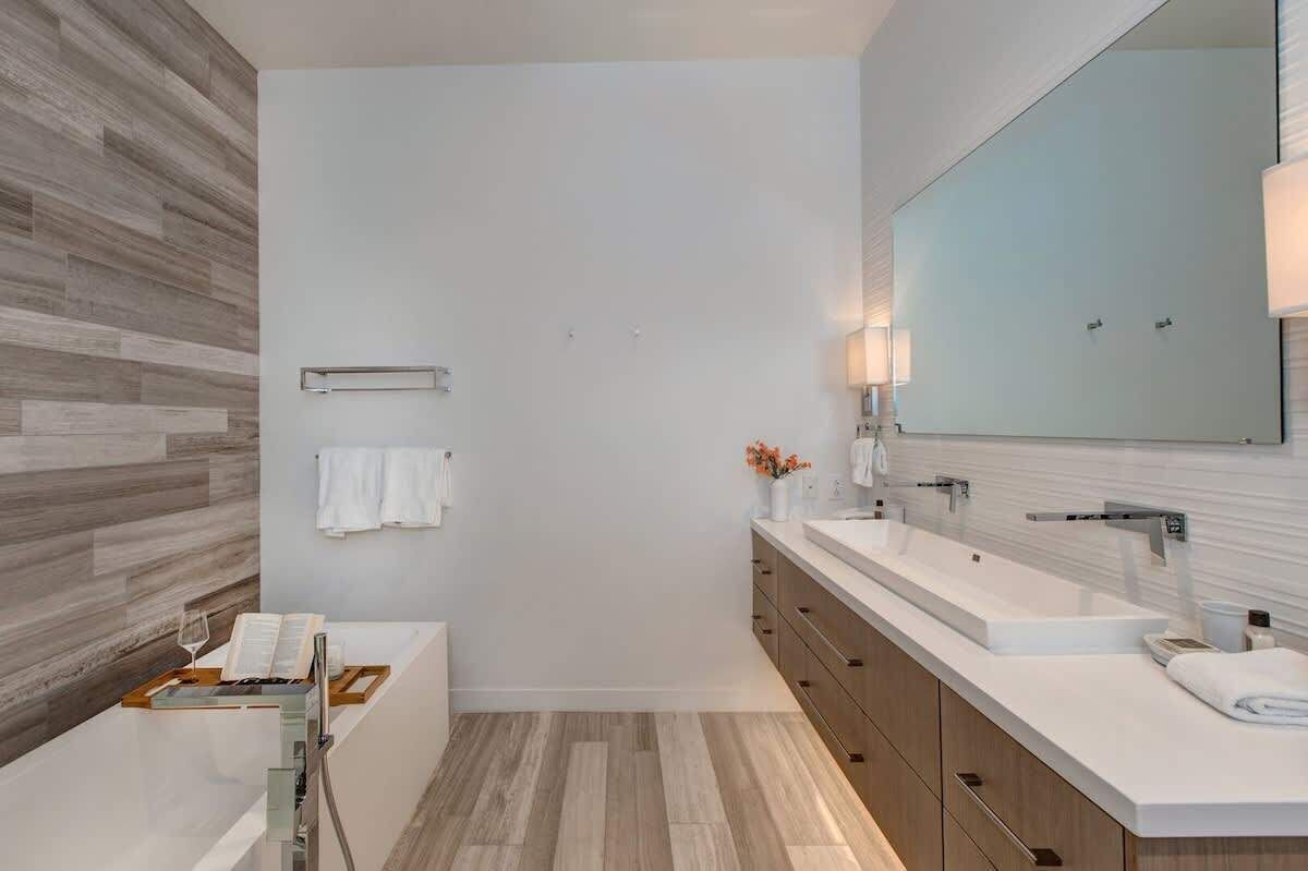 A modern bathroom with a large mirror, two sinks, a bathtub, and a wooden floor.