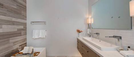 A modern bathroom with a large mirror, two sinks, a bathtub, and a wooden floor.
