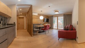 A modern kitchen with a built-in oven, a dining area with a wooden table and red chairs, a red sofa, and a large window with curtains. - Sport Apart (Zell am Ziller)