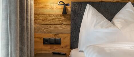 Un dormitorio con pared de madera, una cama con ropa de cama blanca, una mesita de noche con una lámpara y un control remoto sobre la mesa.