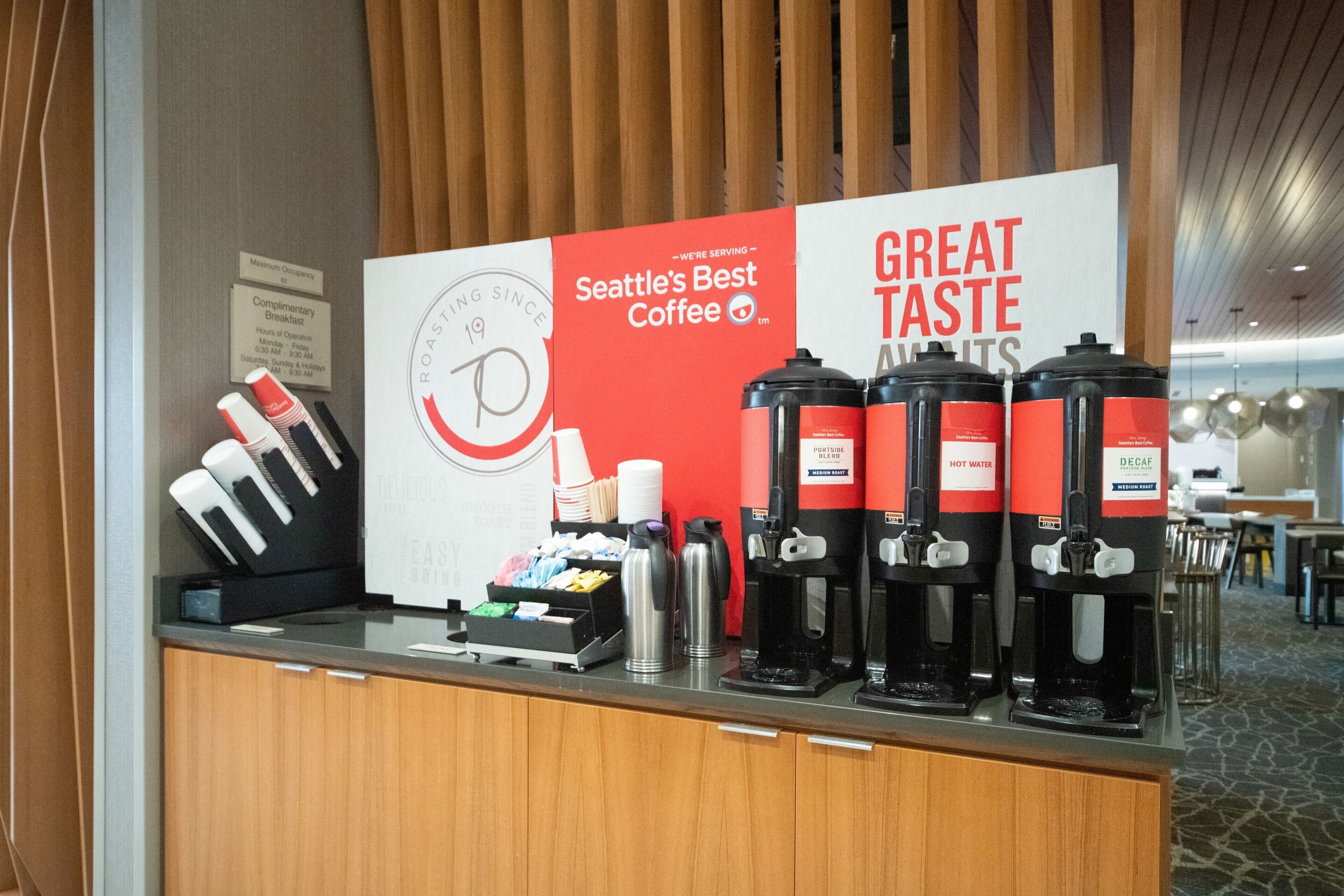 A coffee station with Seattle's Best Coffee branded dispensers, a coffee machine, and various coffee cups and mugs.